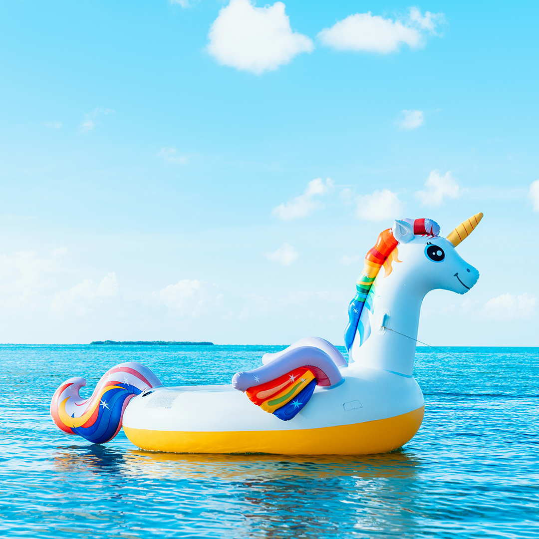 A rainbow unicorn floaty floats on calm water on a beautiful sunny day